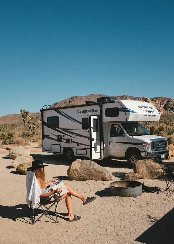 Woman relaxing in a camping chair beside an RV in Joshua Tree, under a big blue sky.