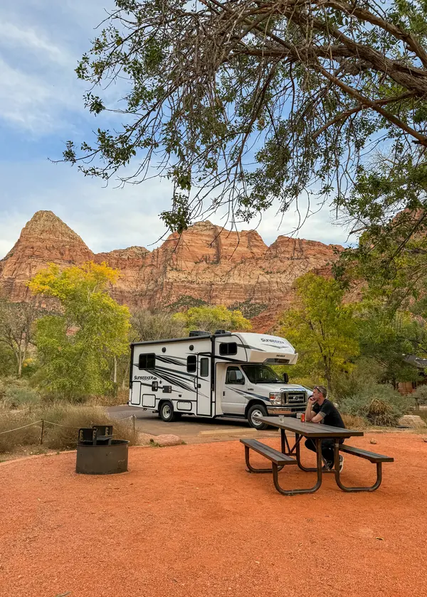 RV and picnic table at a Zion campsite, with autumn trees below red cliffs.
