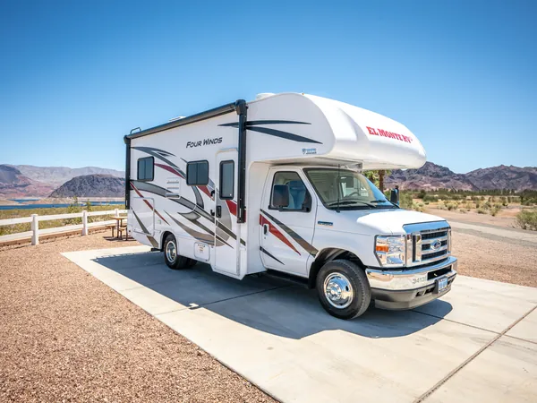 Class C motorhome seen from the front, with desert hills and a lake behind