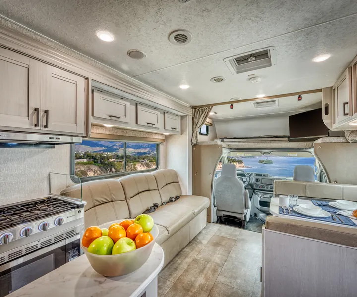 RV kitchen with a stove and a fruit bowl, with the sofa and cab beyond