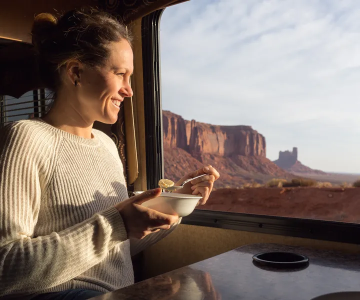 Smiling woman eating breakfast at an RV window that looks out on Monument Valley