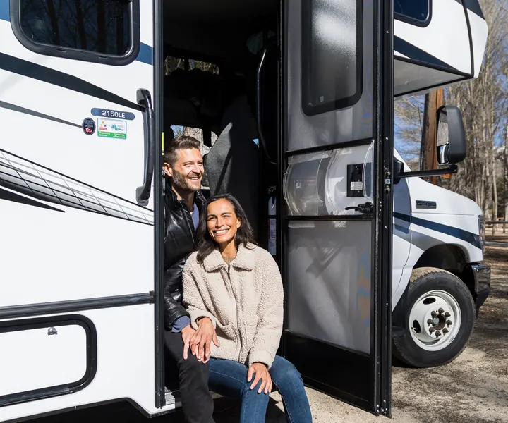 Smiling couple sitting in the doorway of their RV on a sunny day
