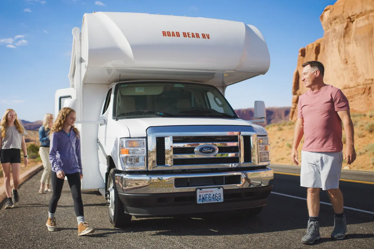 Family walking beside their RV on a canyon road near Moab, below red cliffs