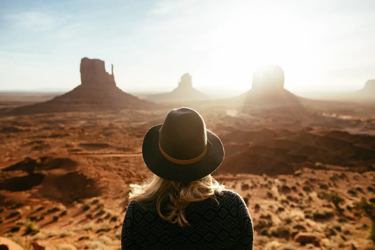 Woman in a hat looking out over the buttes of Monument Valley at sunrise