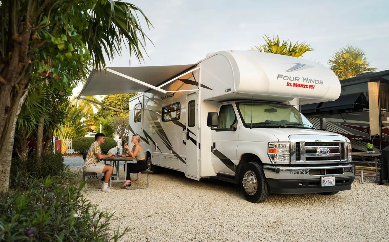 Couple having dinner at a table under the awning of their RV, among palm trees