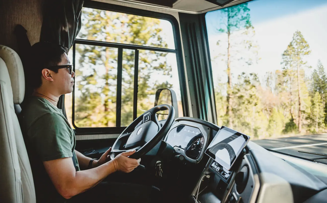 Relaxed driver at the wheel of a motorhome on a sunny forest road