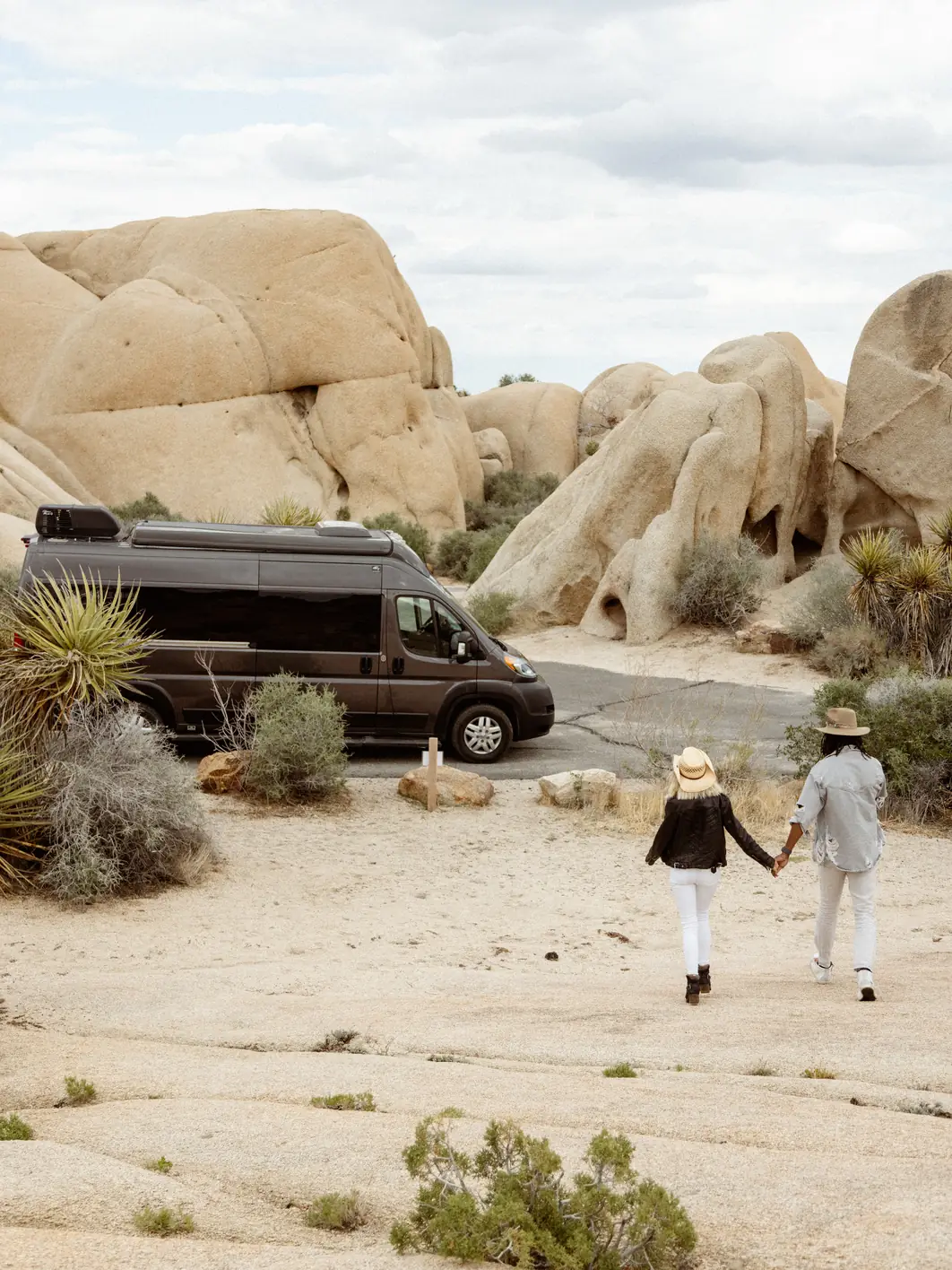 Couple walking hand in hand toward their campervan among granite boulders in Joshua Tree