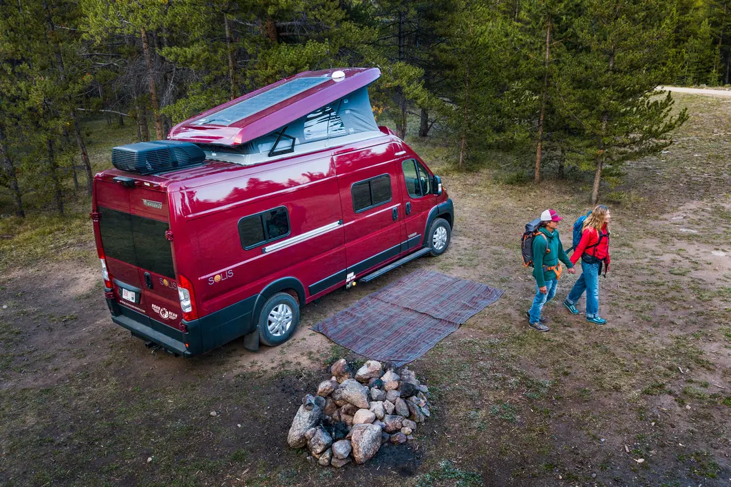 Aerial view of a couple walking back to their red pop-top campervan at a forest campsite