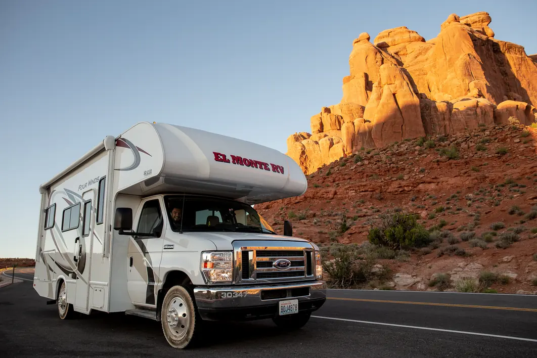 Class C motorhome on a road below glowing red sandstone fins