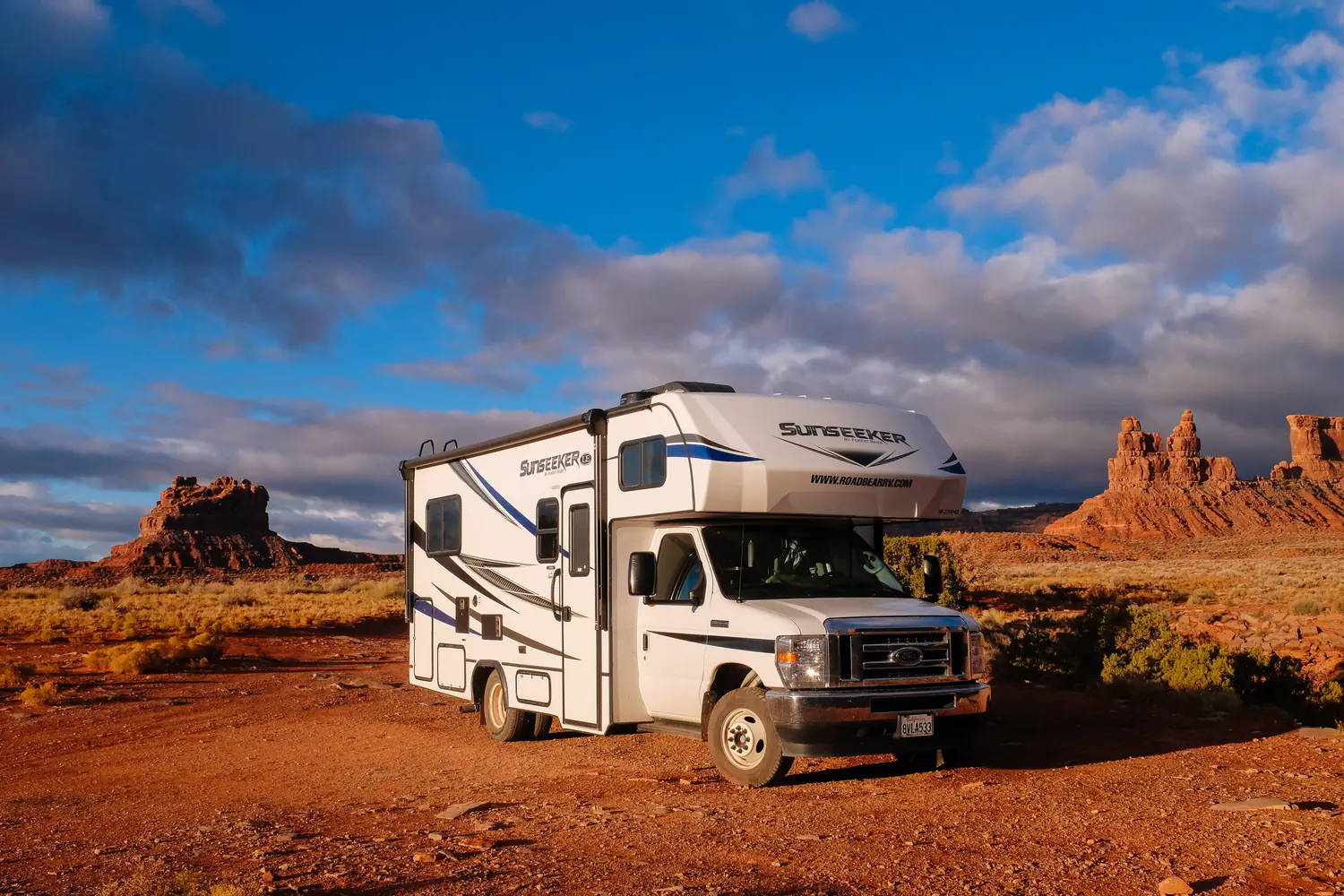 Class C motorhome in warm light in front of red rock towers