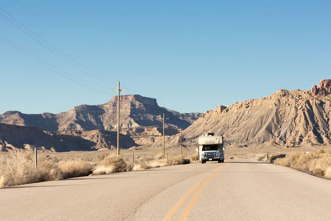 RV approaching on an empty desert road between badlands buttes