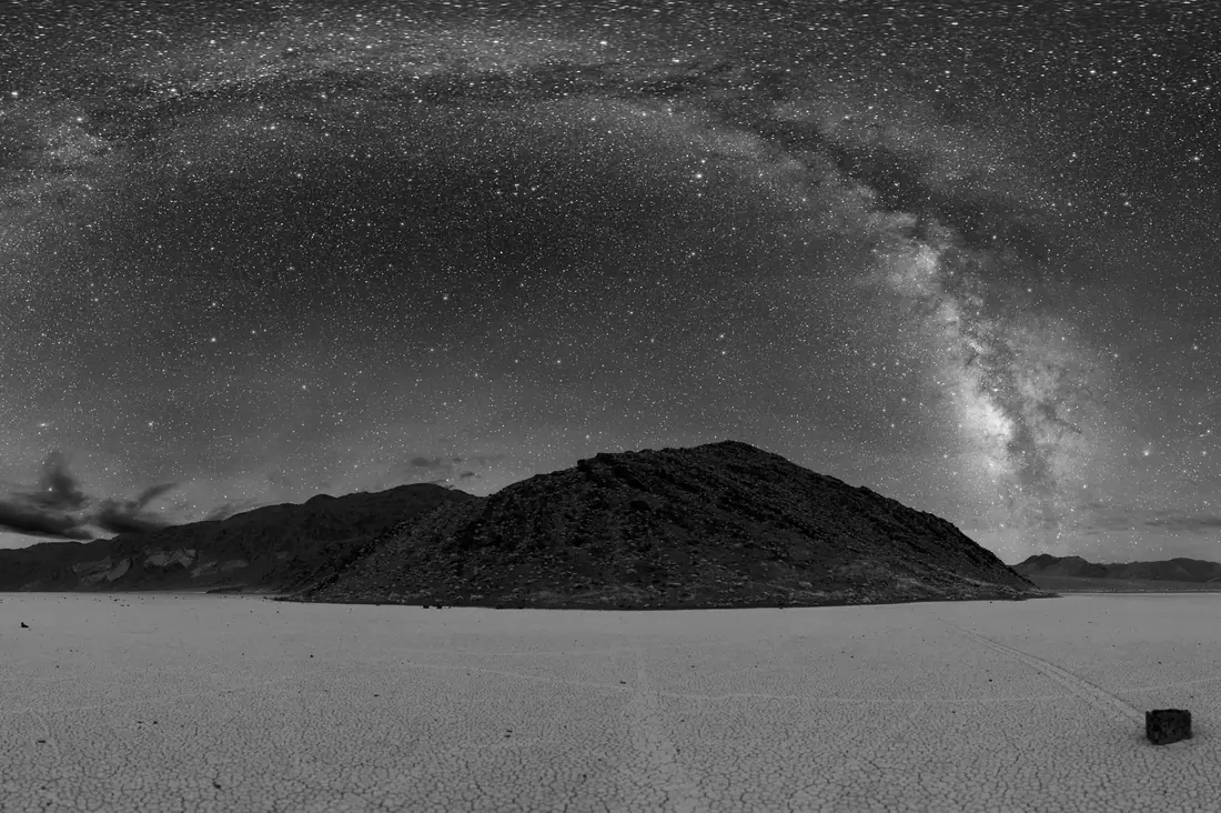 Milky Way arching over a dry lake bed and a dark hill in Death Valley, in black and white