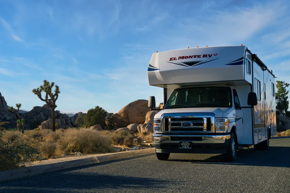 Class C motorhome parked by a desert road among Joshua trees and boulders