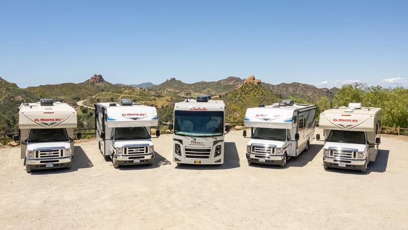 Five rental RVs lined up side by side on a gravel lot under a blue sky