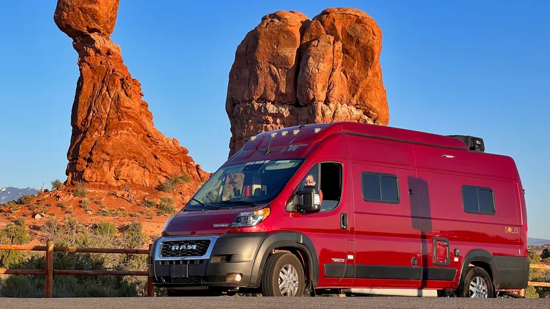 Red campervan parked below Balanced Rock in Arches National Park