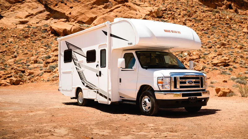 Class C motorhome parked on red sand in front of a glowing sandstone cliff