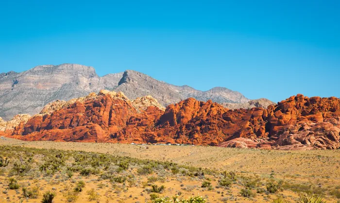 Red sandstone hills below grey limestone mountains at Red Rock Canyon, with desert grassland in front