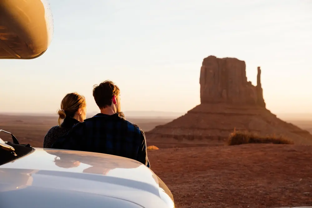 Couple leaning on the hood of their RV, watching the sunrise over a butte in Monument Valley