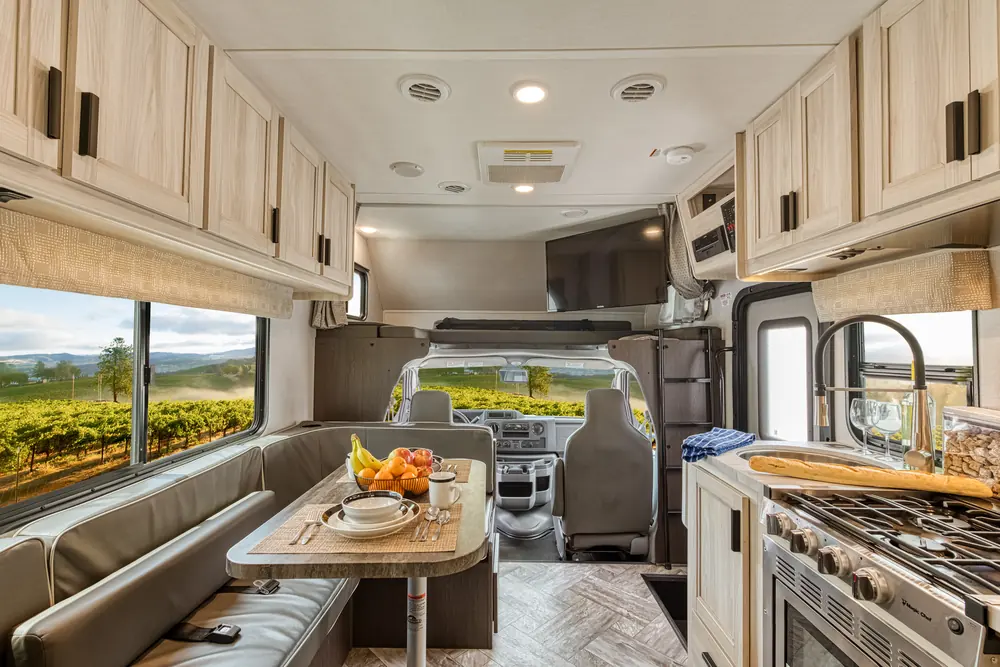 Bright RV interior with a dinette, a kitchen and the cab up front