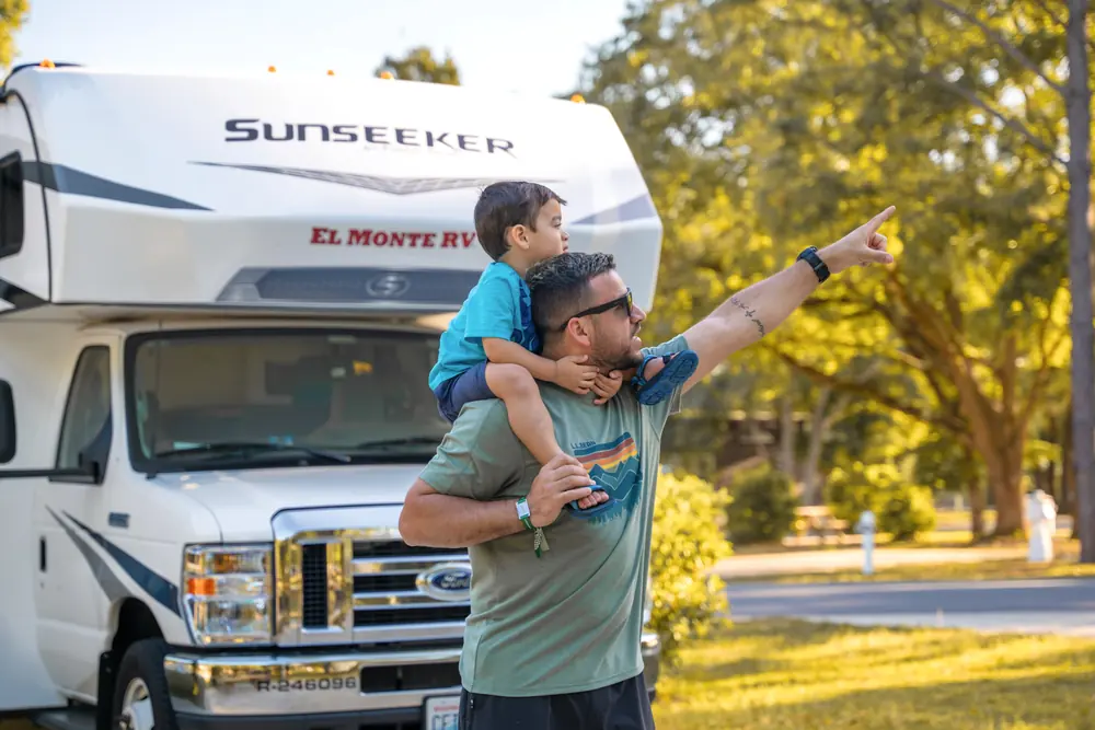 Father with his son on his shoulders pointing ahead, next to their RV
