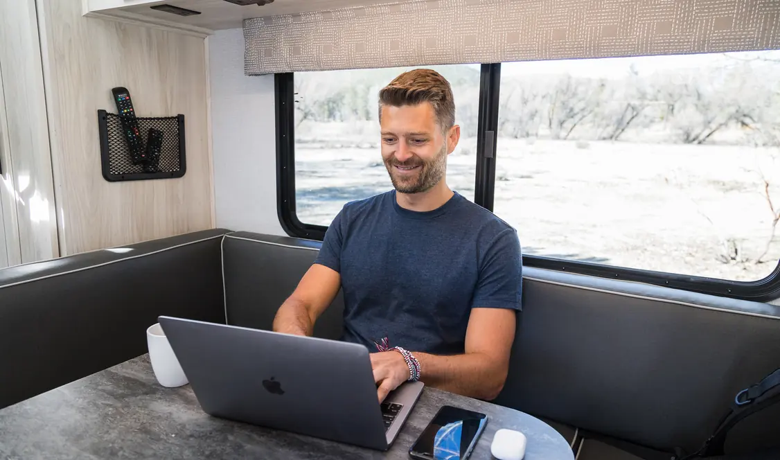 Smiling man using a laptop at the dinette of an RV