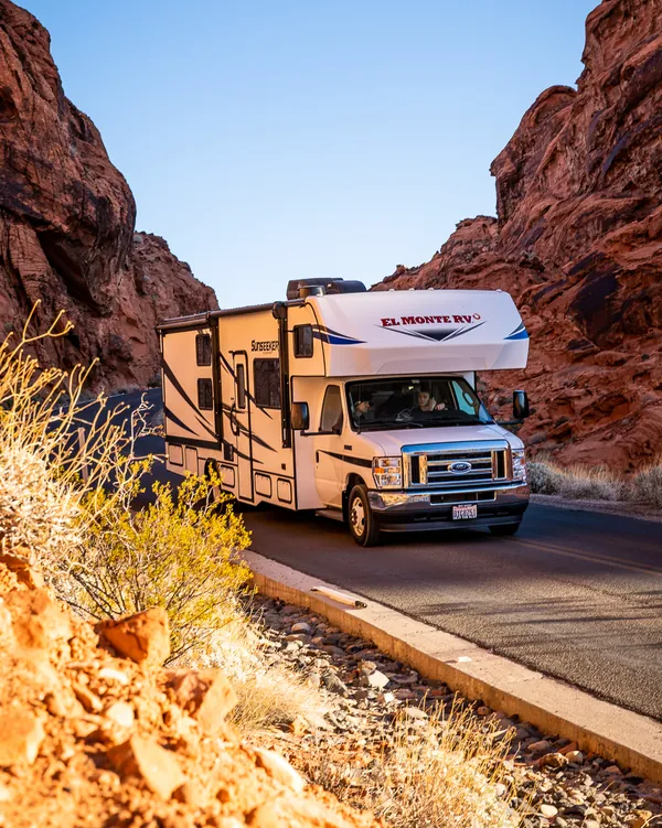 RV driving between towering red sandstone walls on a desert road