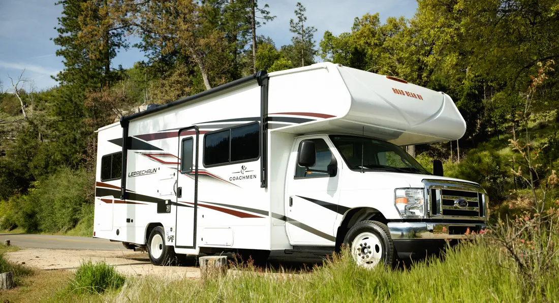 Class C motorhome parked on green grass among pine trees