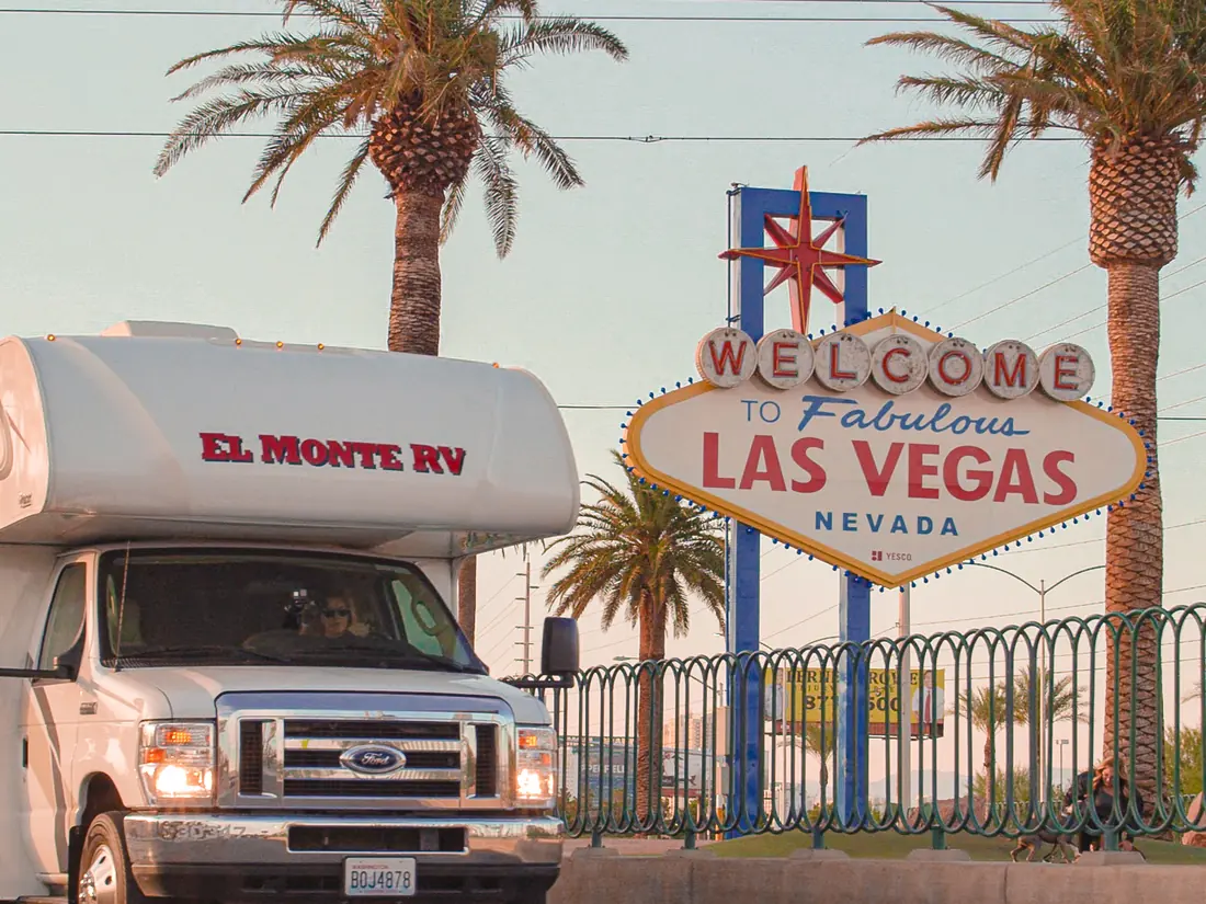 RV parked next to the Welcome to Fabulous Las Vegas sign, between palm trees