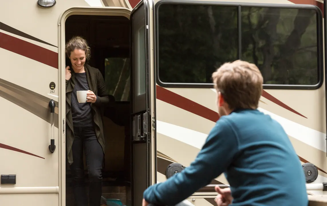 Woman with a mug in the doorway of an RV, chatting with a man outside